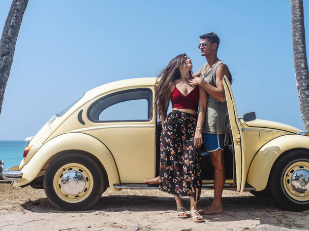 A man and a young woman travel on a vintage car. Palms, ocean beach. - Foto, afbeelding