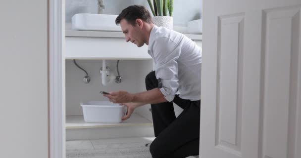 Man Phoning Emergency Plumber After Water Leak At Bathroom, Home. Man At Home Mopping Up Water From Leaking Pipe In Bathroom - Video, Çekim