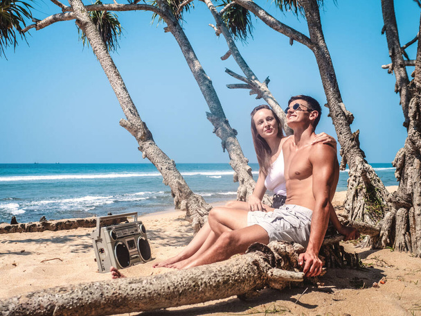Lovers man and woman relax on the tropical beach of Sri Lanka and listen to music from a tape recorder - Fotó, kép