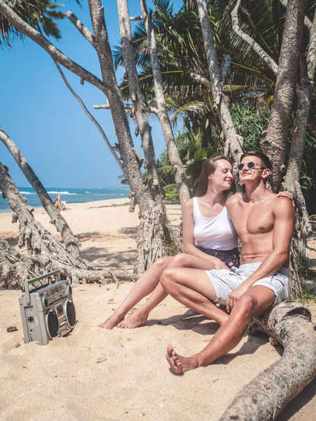 Lovers man and woman relax on the tropical beach of Sri Lanka and listen to music from a tape recorder - Foto, imagen