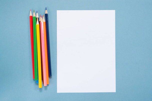 Colorful pencils and blank paper page with copy space on blue background. - Photo, Image