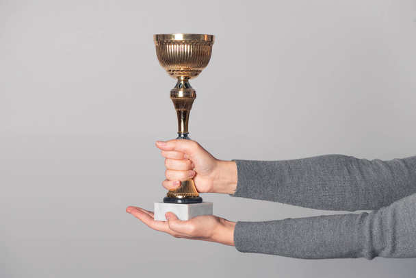 Golden award cup in winner hand isolated on gray background. Award ceremony. - Foto, afbeelding