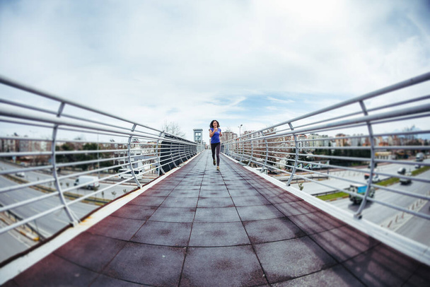 A woman runs across the bridge over the road. Running training in the city. Girl trains endurance. Jogging. Reaching the goal. Workout. City landscape. - Photo, Image
