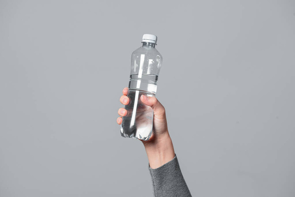 Bottle of water in female hands closeup on gray background. - Photo, Image