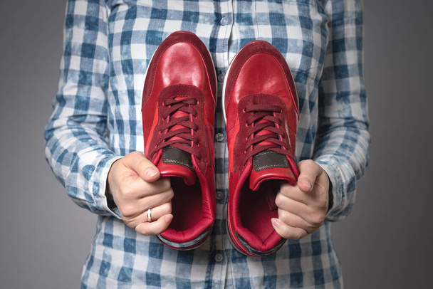 Mujer con un par de nuevos zapatos deportivos rojos en las manos sobre fondo gris
. - Foto, Imagen