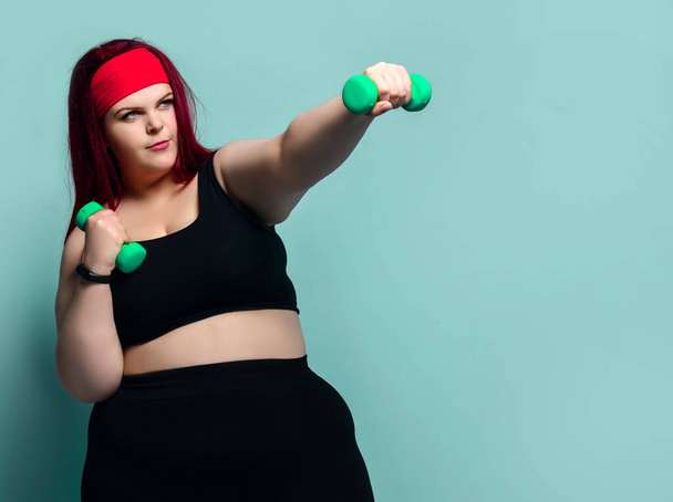 Fitness spring diet weight loss concept. Plus-size overweight woman does punches with dumbbells holding arm outstretched - Foto, imagen