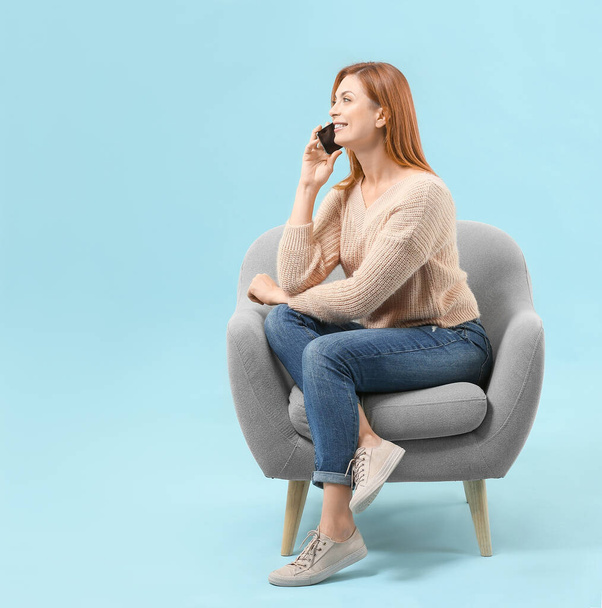 Όμορφη γυναίκα μιλάει στο τηλέφωνο, ενώ κάθεται στην πολυθρόνα με φόντο το χρώμα - Φωτογραφία, εικόνα