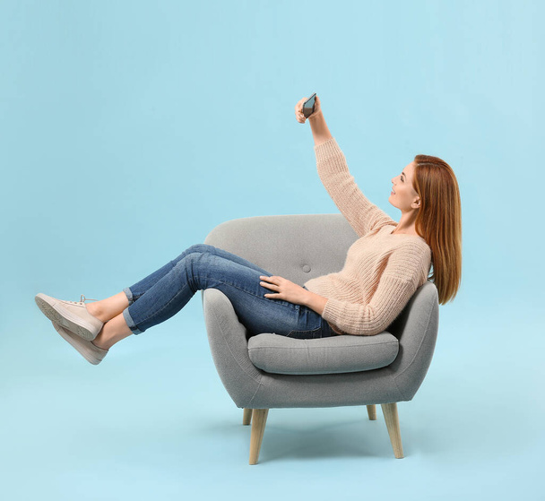 Mulher bonita tomando selfie enquanto sentado em poltrona contra fundo de cor
 - Foto, Imagem