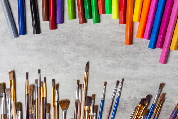 Paint brushes and multi-colored markers scattered on the table, drawing tools top view on a gray background, copy space, close-up - Photo, Image