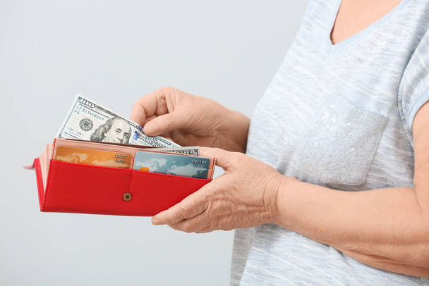 Senior woman with wallet and money on light background - Photo, Image
