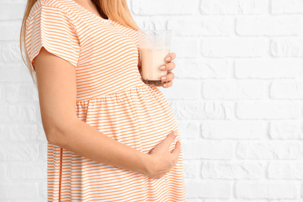 Hermosa mujer embarazada con leche sobre fondo de ladrillo blanco
 - Foto, imagen