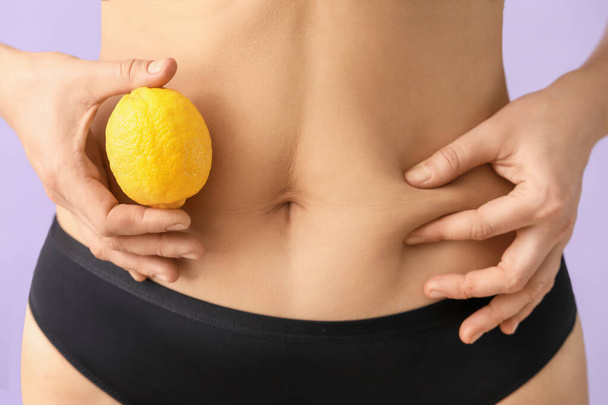 Young woman with cellulite problem and lemon on color background, closeup - Φωτογραφία, εικόνα