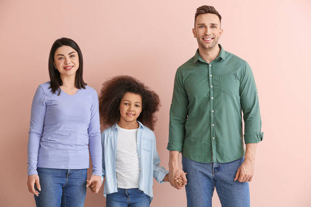 Glückliches Paar mit wenig Adoptivmädchen auf farbigem Hintergrund - Foto, Bild