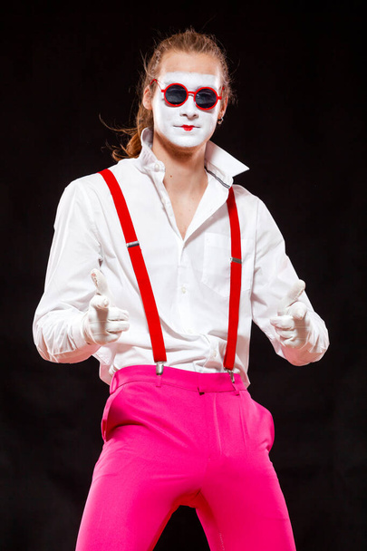 Portrait of male mime artist, isolated on black background. Man in suspenders and pink trousers is posing pointing at his viewer with confident look - Photo, Image