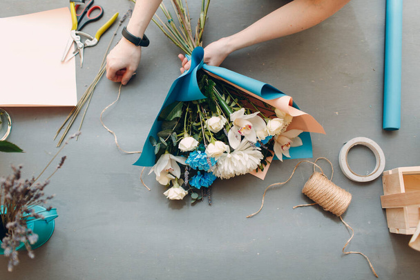 Florista faz um buquê em uma butique de flores na vista superior da mesa cinza
 - Foto, Imagem