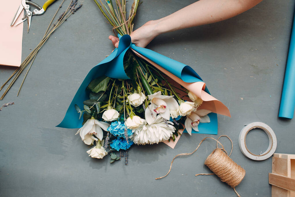 Bloemist maakt een boeket in een bloem boetiek op grijze tafel bovenaanzicht - Foto, afbeelding