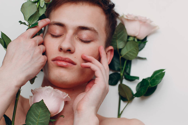 Fiatal férfi modell virágokkal. Szépségportré. Friss, sima bőr érintése. - Fotó, kép