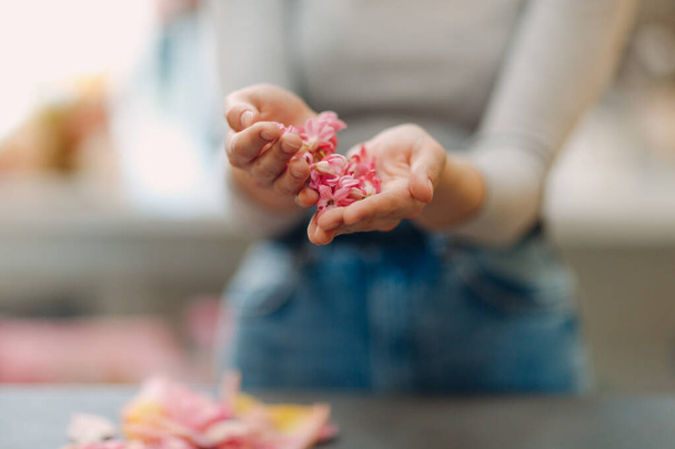 Weibliche Hände und rosa Blumen und Blütenblätter in den Handflächen. - Foto, Bild