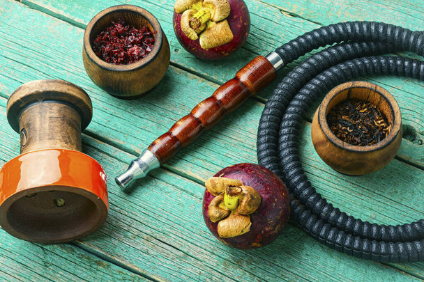 Narguilé fumeur asiatique avec tabac shisha avec saveur de mangoustan. Tabac nargile aux fruits sur fond bois
. - Photo, image