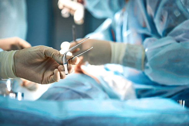 Τα χέρια των χειρουργών κρατούν ένα χειρουργικό εργαλείο στο χειρουργείο. Κοντινό πλάνο, όμορφο φως, σύγχρονη ιατρική, σώζοντας ζωές. - Φωτογραφία, εικόνα