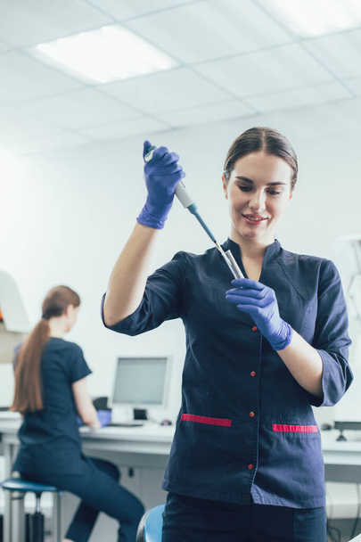 Cheerful lab technician working with an auto-pipette dispenser and smiling - Photo, image