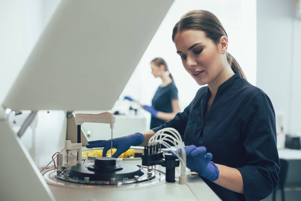 Attentive woman switching on a modern machine in the laboratory - 写真・画像