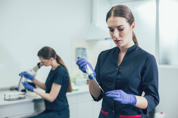 Calm lab assistant wearing rubber gloves and carefully holding a microscope slide - Foto, Imagem