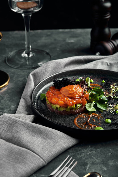 Tártaro de salmón con aguacate en un plato oscuro, Cocina italiana tradicional, plato sobre fondo oscuro, bajo tono con espacio para copiar
 - Foto, imagen