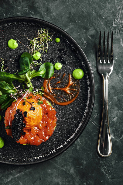 Salmon tartare with avocado on a dark plate, Traditional Italian cuisine, dish on a dark background, low key with copy space - Photo, Image