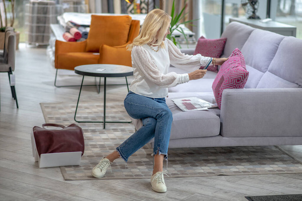Woman sitting on a sofa photographing a pink pillow. - Фото, зображення