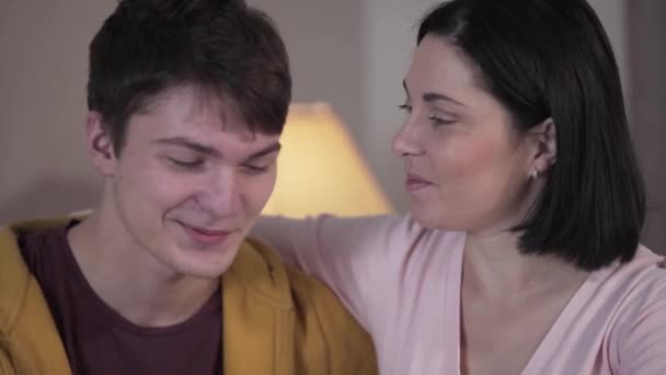 Close-up faces of young Caucasian mother and teenage son talking, looking at camera and smiling. Portrait of happy woman and boy posing indoors. Happiness, unity, lifestyle. - Footage, Video