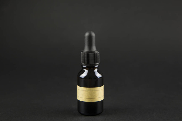 Botella de pipeta marrón sobre fondo negro con etiqueta marrón en blanco, rellene usted mismo
. - Foto, imagen