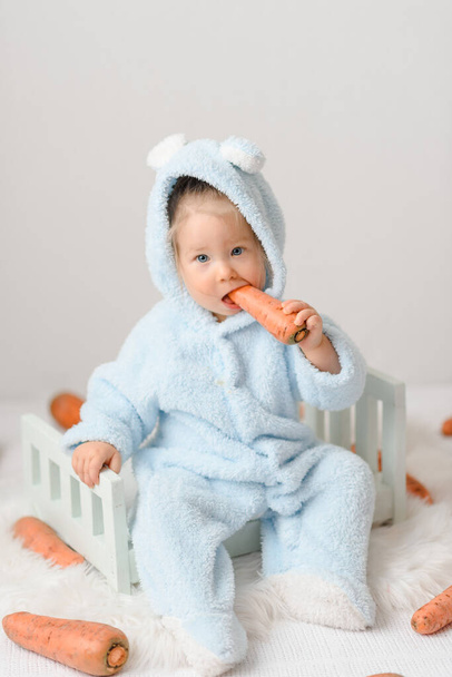 Ένα κοριτσάκι με στολή λαγού τρώει ένα καρότο. Υγιεινός τρόπος ζωής. Το πρώτο δέλεαρ του παιδιού - Φωτογραφία, εικόνα