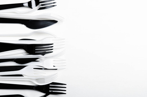 Plastové bílé a černé jednorázové vidlice a nože na bílém pozadí. Plastová jídla. Kopírovat prostor, horní pohled, byt ležel - Fotografie, Obrázek