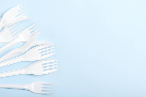 Plastic white disposable forks and knives on a blue background. Concept plastic dishes, fast food, plastic pollution. Copy space, top view, flat lay - Φωτογραφία, εικόνα