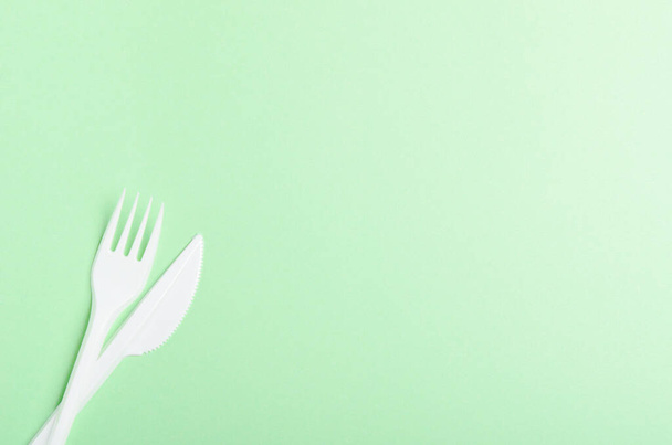 Plastic fork and knife on a green background. Concept plastic dishes, plastic pollution. Copy space, top view, flat lay - Foto, Bild