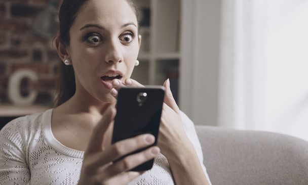 Young shocked woman receiving an incredible surprise on her smartphone - Photo, Image