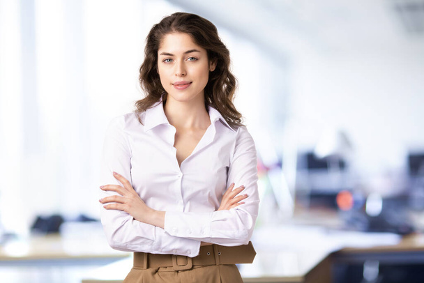 Портрет молодой предпринимательницы, стоящей со скрещенными руками и улыбающейся стоя в офисе
. - Фото, изображение