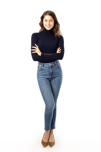 Full length shot of smiling young woman wearing turtlenck sweater and blue jeansi while standing at isolated white background.  - Φωτογραφία, εικόνα