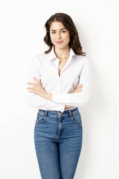 Portrait shot of attractive young woman wearing white shirt while standing with arms crossed at isolated white background. - Φωτογραφία, εικόνα