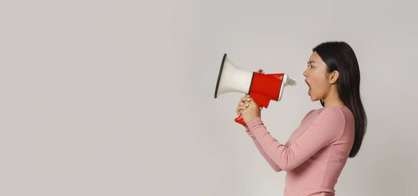 Emotional asian woman shouting in megaphone over grey background - Photo, Image