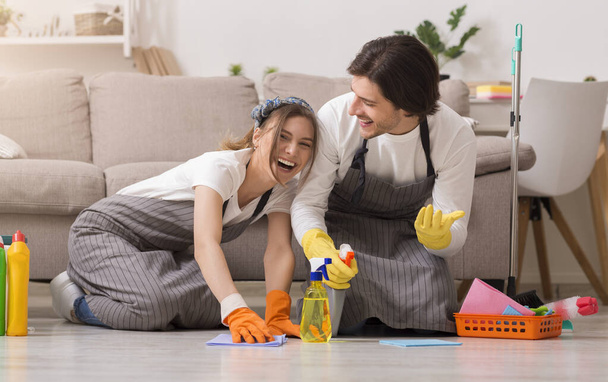 Limpia de primavera. Pareja joven divirtiéndose mientras limpian la casa, lavando el piso juntos
 - Foto, Imagen