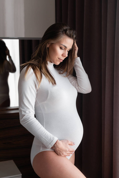 early pregnancy. Young beautiful girl in expectation of a child stands at a large window. seventh month of expectation of the child. Expectant mother communicates with the fetus. - Valokuva, kuva