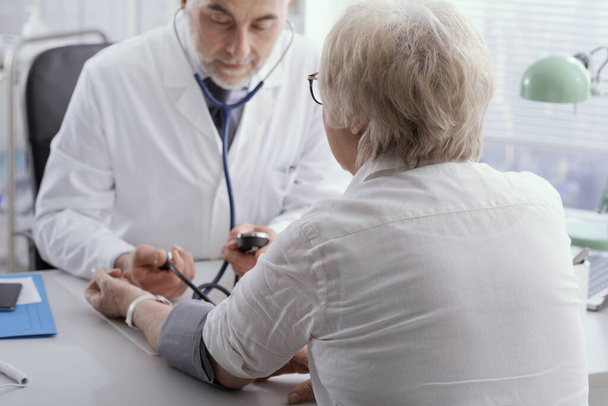 Επαγγελματίας ιατρός που μετρά την αρτηριακή πίεση μιας ηλικιωμένης γυναίκας ασθενούς κατά τη διάρκεια επίσκεψης, υπέρτασης και πρόληψης - Φωτογραφία, εικόνα