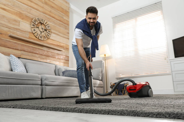 Young man using vacuum cleaner at home - Foto, afbeelding