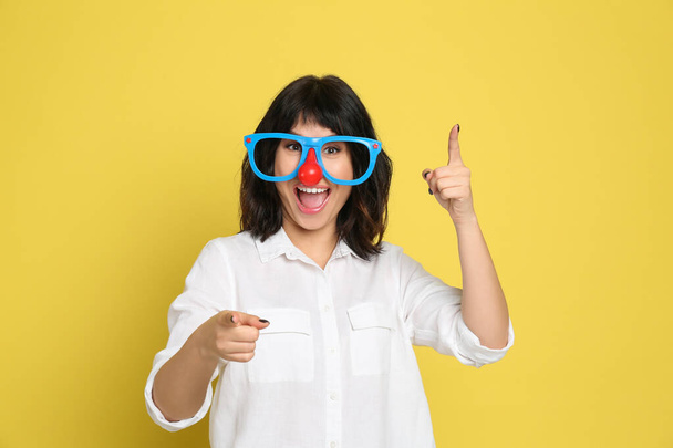 Joyful woman with funny glasses on yellow background. April fool's day - Photo, image
