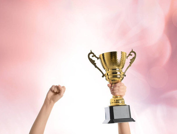 Woman holding gold trophy cup on color background, closeup - Photo, Image