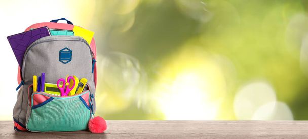 Bright backpack with school stationery on table against blurred green background. Space for text - Fotó, kép