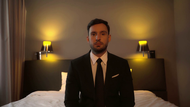 biznesmen w garniturze siedzi na łóżku w pokoju hotelowym  - Materiał filmowy, wideo