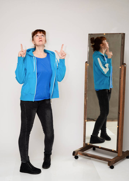 Full-length photo woman with emotions in a medical color mask in front of a mirror on a white background - Photo, image